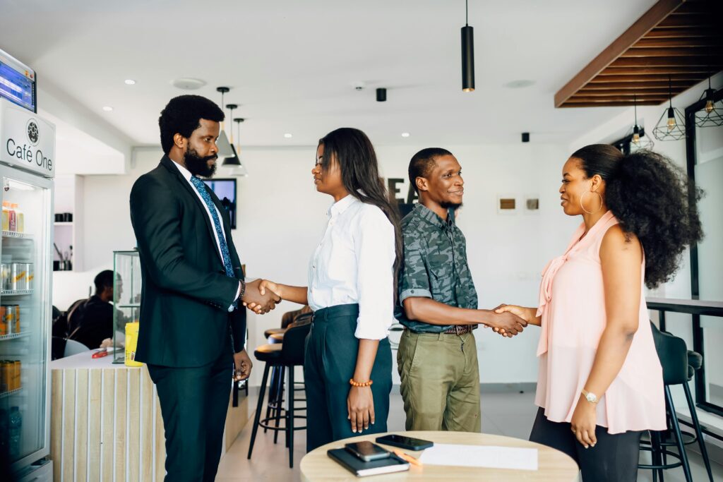 Four adults engage in a professional handshake at a cafe in Lagos, Nigeria, showcasing teamwork and collaboration.